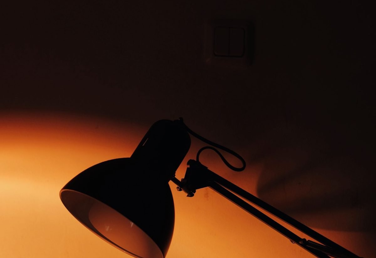 Desk lamp silhouetted against warm light in a dark room