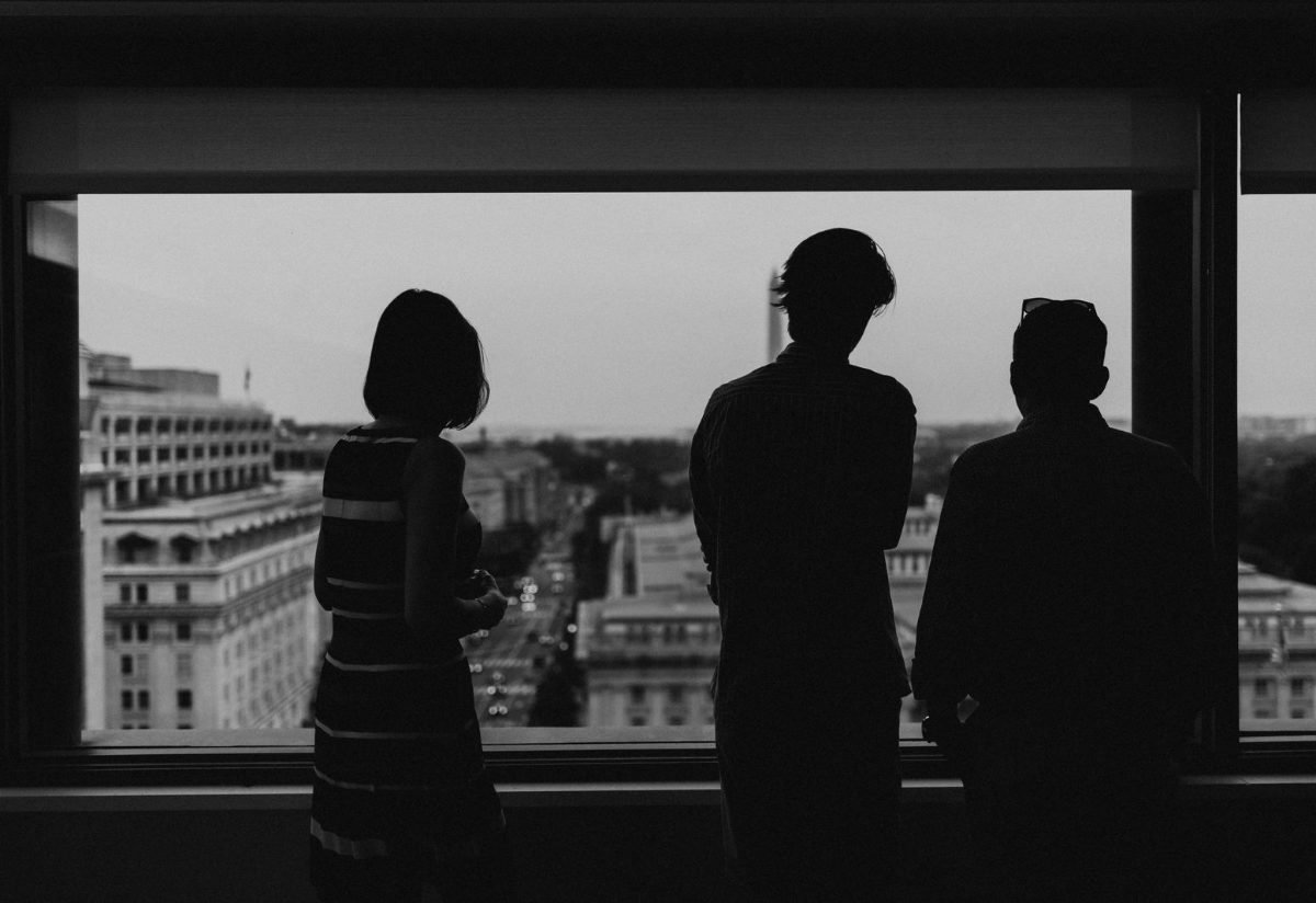 Three silhouettes reviewing a city view from an office window
